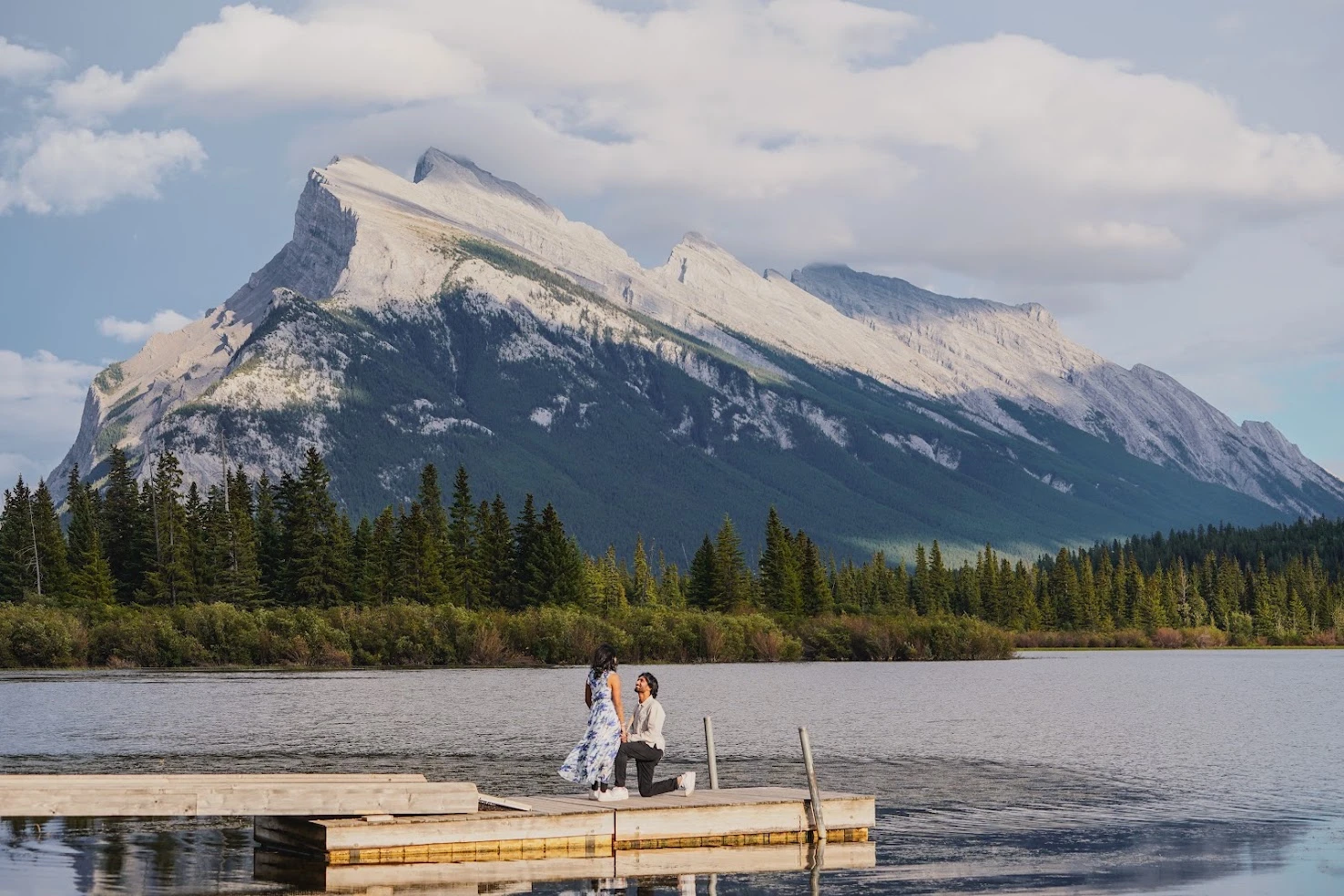 Shan proposing to Neha on a dock by a mountain lake
